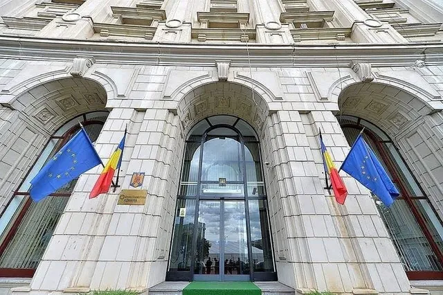 O clădire de piatră cu trei arcuri mari prezintă trei steaguri și o intrare cu uși de sticlă.