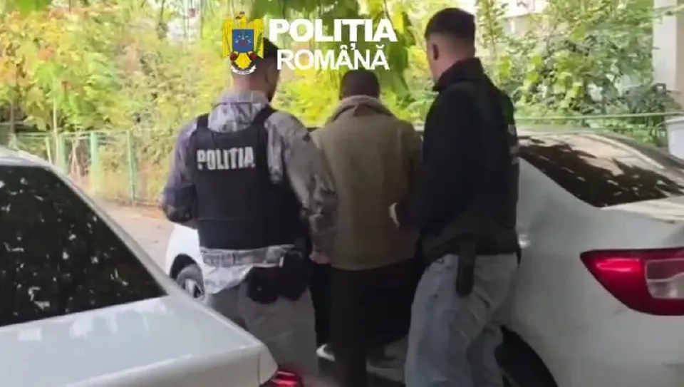 Trei bărbați stau lângă două mașini albe, dintre care doi poartă veste negre cu inscripția POLITIA.
