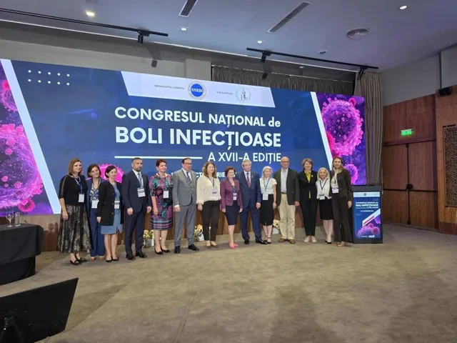 Un grup de persoane stă în rând pe o scenă în fața unui ecran mare care afișează un text despre un congres de boli infecțioase.
