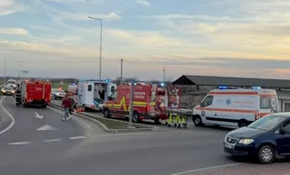 Mai multe vehicule de serviciu, inclusiv ambulanțe și o autospecială de pompieri, sunt parcate pe o porțiune de drum asfaltat sub un cer înnorat.