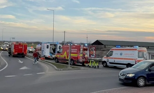 Mai multe vehicule de serviciu, inclusiv ambulanțe și o autospecială de pompieri, sunt parcate pe o porțiune de drum asfaltat sub un cer înnorat.