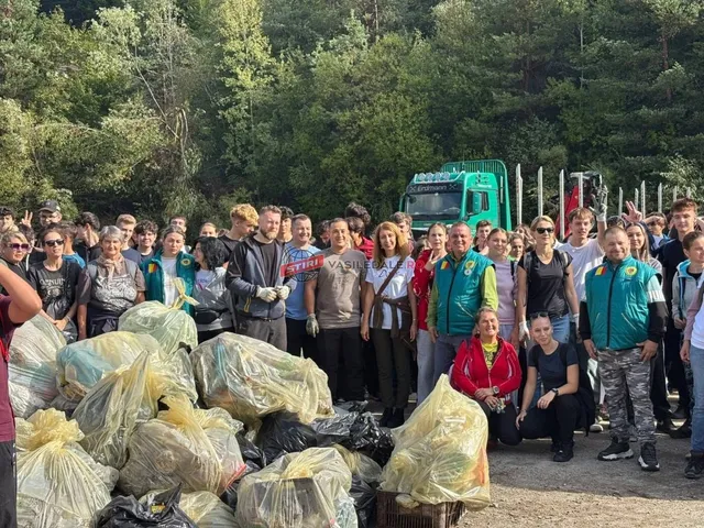 Un grup de oameni stă lângă saci mari de gunoi plini, într-o zonă deschisă cu copaci în fundal.
