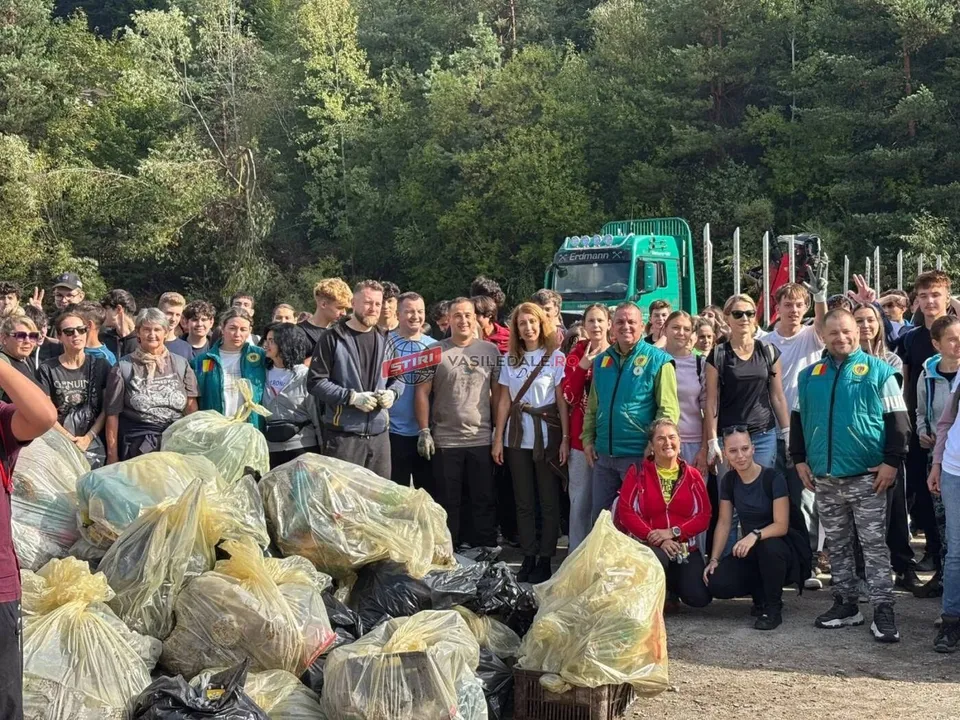 Un grup de oameni stă lângă saci mari de gunoi plini, într-o zonă deschisă cu copaci în fundal.