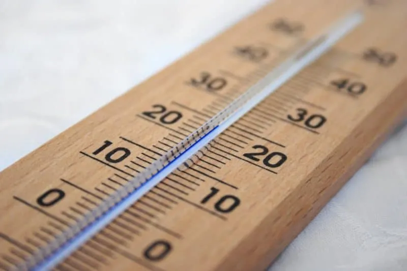 Un termometru de lemn cu o scală numerică de la zero la patruzeci este așezat pe o suprafață albă.