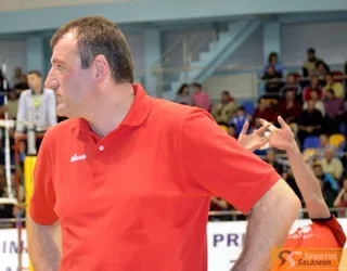 Un bărbat cu tricou polo roșu stă în prim-plan, în timp ce mâini cu degete întinse apar în partea dreaptă a imaginii.