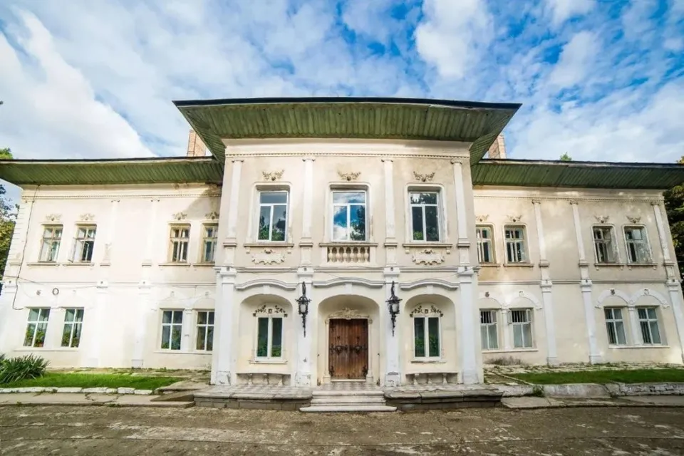 O clădire albă cu două etaje, dotată cu ferestre multiple și un acoperiș lat, este situată sub un cer cu nori albi.