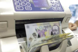 Banii în bancnote sunt introduși într-un aparat de numărat bani de culoare albă.