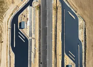 O vedere aeriană prezintă o autostradă cu două benzi, flancată de zone de asfalt negru și terenuri de culoarea nisipului.