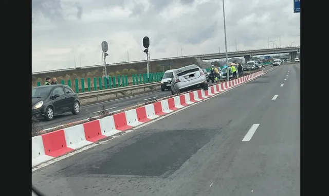 Un autoturism gri este înclinat peste o barieră de beton formată din elemente albe și roșii, pe un drum cu mai multe benzi de circulație.