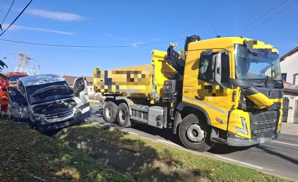 Un camion galben și un microbuz alb cu partea frontală avariată sunt oprite pe marginea unui drum lângă o zonă cu vegetație.