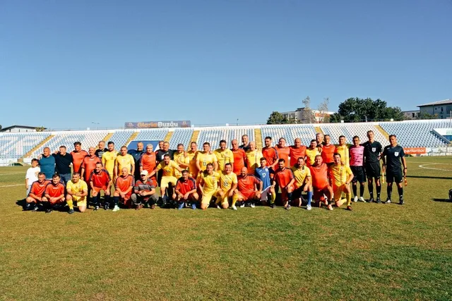 Un grup de bărbați în echipamente sportive colorate stau poziționați pe un teren de fotbal verde sub un cer senin.