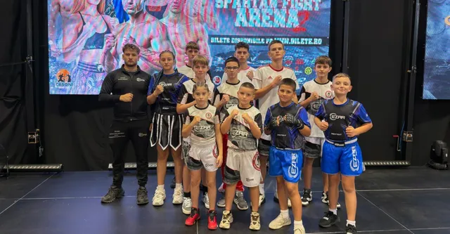 Un grup de copii și un adult stau în picioare în fața unui ecran mare, purtând echipamente sportive și echipamente de protecție.