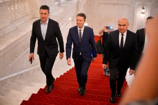 Trei bărbați în costume scurte coboară pe o scară acoperită cu un covor roșu.