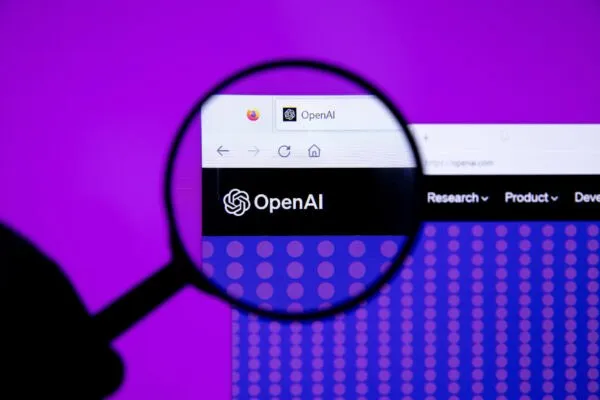 O lupă este poziționată deasupra unui ecran de computer care afișează logo-ul OpenAI pe un fundal violet cu puncte luminoase.