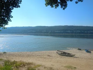Un râu lat curge sub un cer senin, având o rive nisipoasă în prim-plan cu o barcă mică și vegetație pe margini.