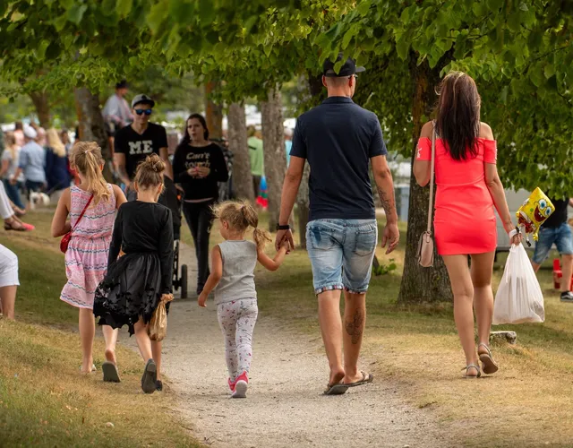 O grupă de persoane merge pe un drum de pământ printre copaci, printre care se află un bărbat în tricou negru și două femei.
