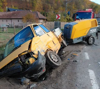 Un autoturism galben este răsucit pe o parte, având partea frontală zdrobită, lângă o autoutilitară galbenă cu numărul 720 pe marginea drumului.