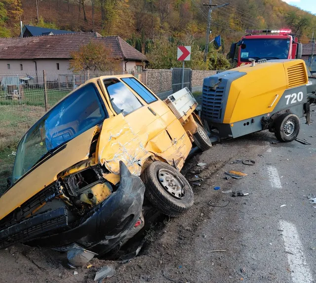 Un autoturism galben este răsucit pe o parte, având partea frontală zdrobită, lângă o autoutilitară galbenă cu numărul 720 pe marginea drumului.