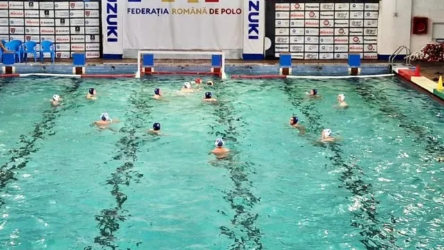 Oameni cu căciuli de înot înoată într-o piscină interioară cu linii negre pe fundul cu apă turcoaz, sub un banner al unei federații de polo.