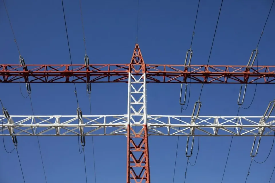 O structură metalică de înaltă tensiune, vopsită în alb și roșu, este dispusă sub un cer albastru intens.