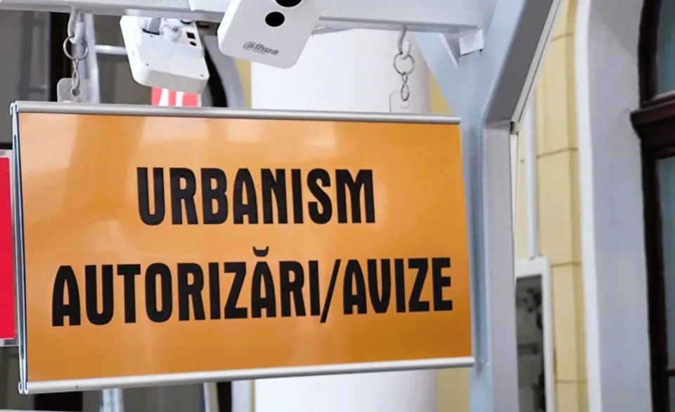 Un afiș dreptunghiular galben cu textul negru URBANISM AUTORIZĂRI/AVIZE este suspendat sub un suport alb.