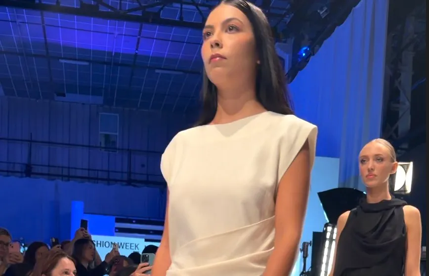 O femeie cu părul lung și negru poartă o rochie albă fără mâneci, în timp ce o altă femeie cu părul scurt poartă o rochie neagră.