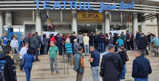 O mulțime de oameni stă în fața unei clădiri cu un afiș care menționează bursa locurilor de muncă.