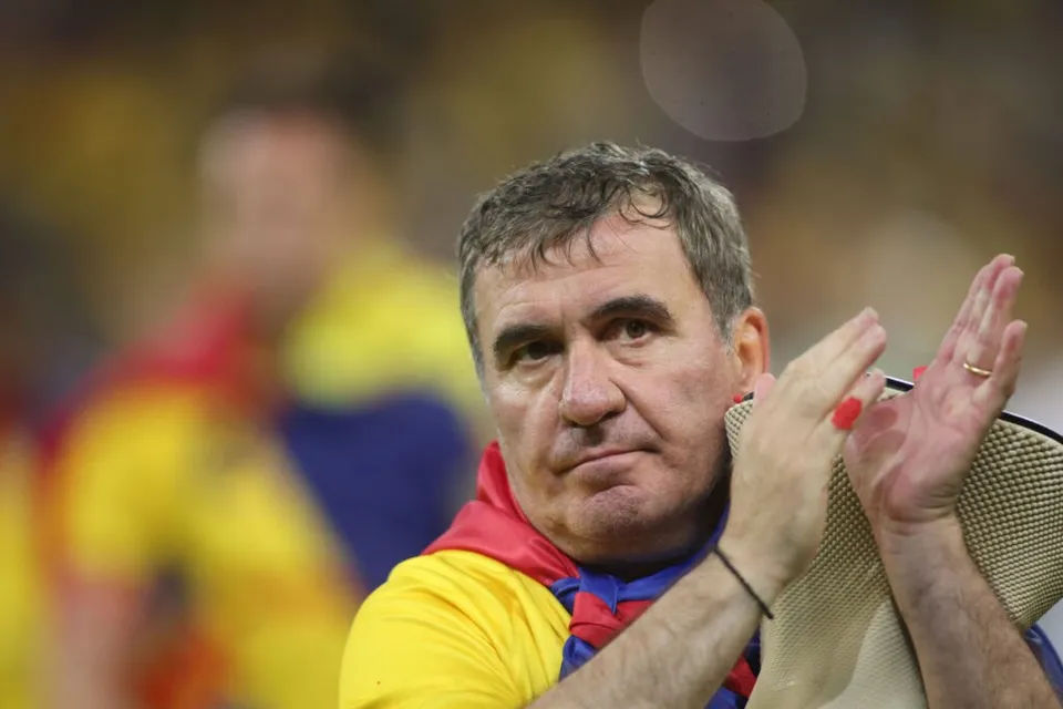 Un bărbat cu părul scurt și grijit aplaudă, purtând un tricou galben cu detalii roșii și albastre.