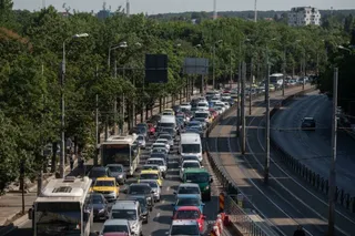 O mulțime de mașini și autobuze circulă pe mai multe benzi de drum într-o zonă urbană cu copaci de-a lungul drumului.