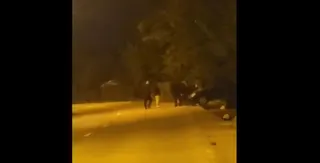 Mai multe siluete de persoane sunt vizibile pe o stradă iluminată noaptea lângă un vehicul parcat.
