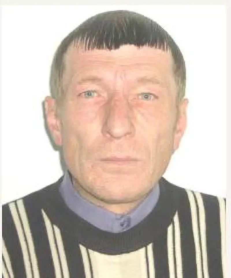 Un bărbat cu păr scurt și deschis la culoare poartă un tricou cu dungi verticale negre și albe peste o cămașă de culoare violet.