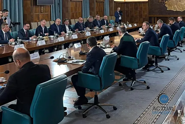 Oamenii în costume purtând cămăși albe stau la o masă lungă de conferință într-o sală cu pereți din lemn.