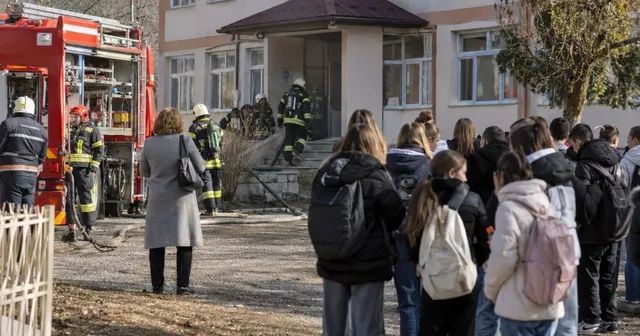 Pompieri în echipament de protecție și un grup de persoane cu rucsacuri stau pe o curte lângă o clădire și un autospecială de stingere.