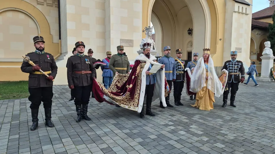 Oameni îmbrăcați în costume istorice stau pe o esplanadă pavată în fața unei clădiri cu arcade mari.