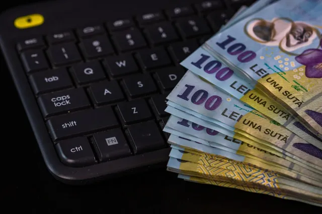 Un tastatură neagră este așezată lângă un teanc de bancnote de o sută de lei.