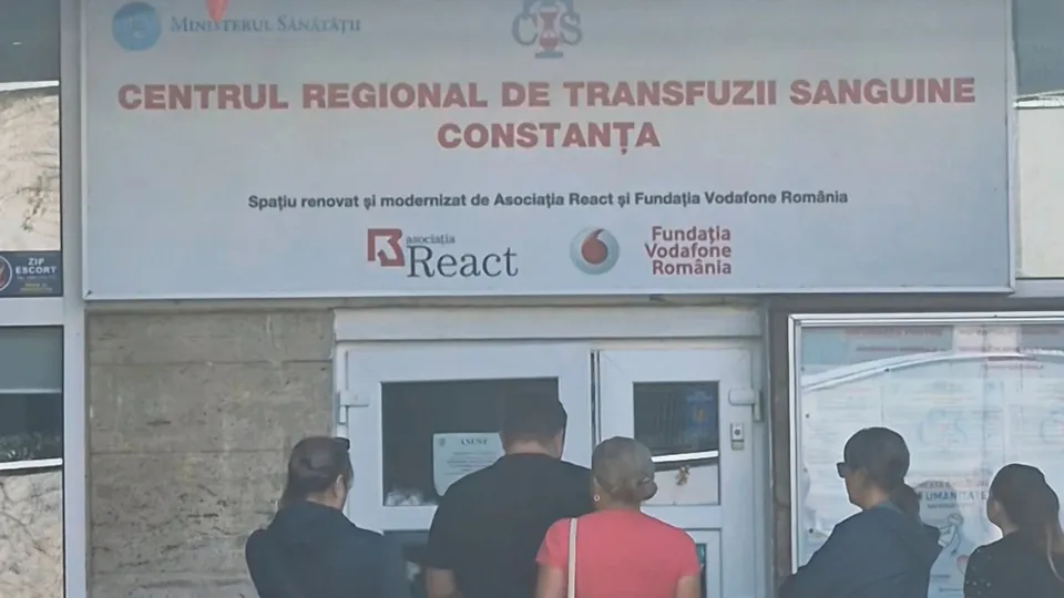 Oamenii stau în fața unei clădiri sub un panou informativ care indică Centrul Regional de Transfuzii Sanguine Constanța.