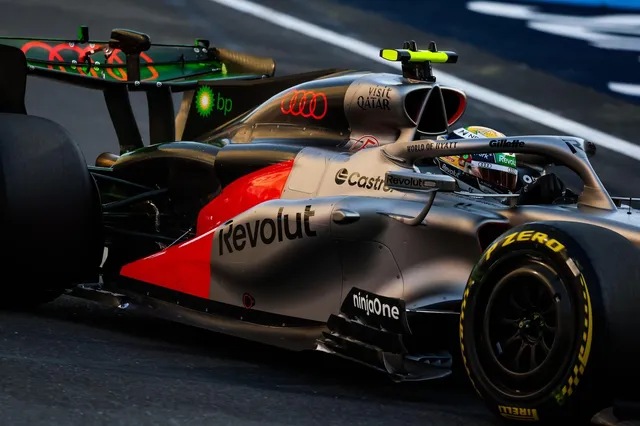 Un monopost de Formula 1 de culoare gri și roșu circulă pe o pistă de curse, având diverse logouri de sponsorizare pe caroserie și pneuri.
