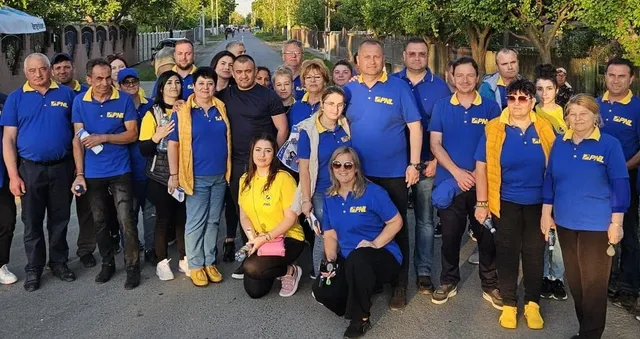 Un grup de oameni stă pe un drum, mulți purtând tricouri albastre cu inscripții galbene.