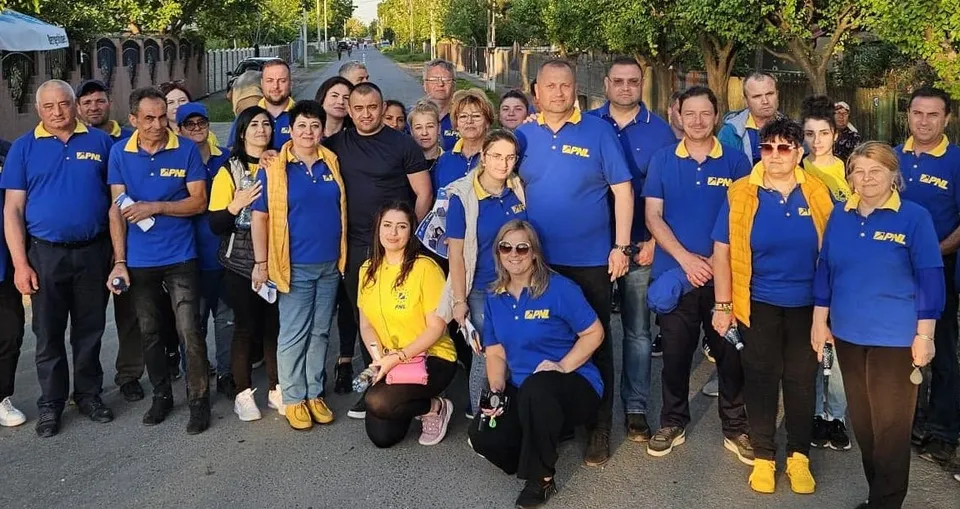 Un grup de oameni stă pe un drum, mulți purtând tricouri albastre cu inscripții galbene.