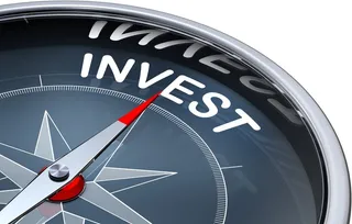 O busolă cu cadran negru prezintă cuvântul INVEST scris cu litere albe și o acul gri cu vârful roșu.