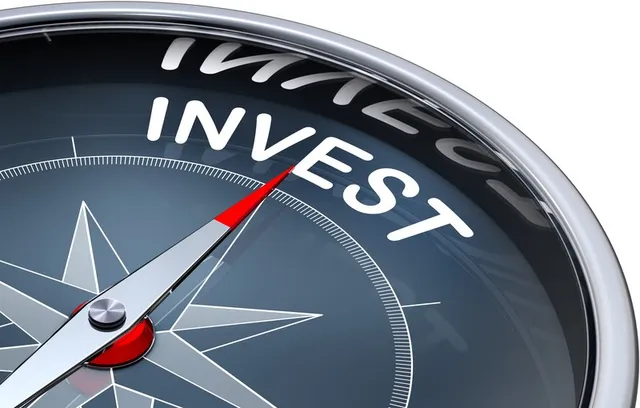 O busolă cu cadran negru prezintă cuvântul INVEST scris cu litere albe și o acul gri cu vârful roșu.