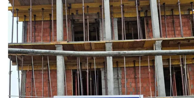 O structură de beton cu pereți din cărămidă roșie este susținută de stâlpi metalici și grinzi de lemn pe mai multe niveluri.