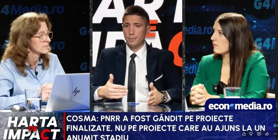 Trei persoane stau la o masă într-un studio, un bărbat în costum și cravată fiind încadrat între două femei.
