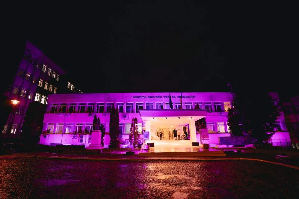 O clădire de mai multe etaje este iluminată cu o lumină roz intensă pe fundalul unui cer de noapte întunecat.