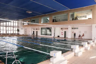 O piscină interioară cu linii de delimitare pe apă, cu blocuri de start albe pe marginea bazinului și ferestre mari în fundal.