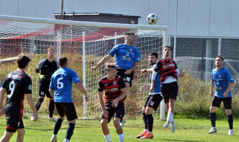 Cei opt jucători de fotbal de pe teren sunt îmbrăcați în echipamente de sport de culori albastre sau negre cu detalii roșii pe un teren de iarbă.
