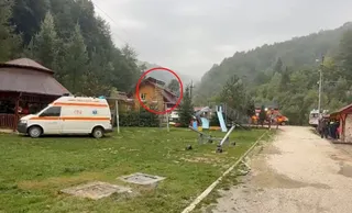 O dubă albă cu inscripții roșii este parcată pe un teren de iarbă lângă o clădire cu acoperiș în formă de con și un teren de joacă.