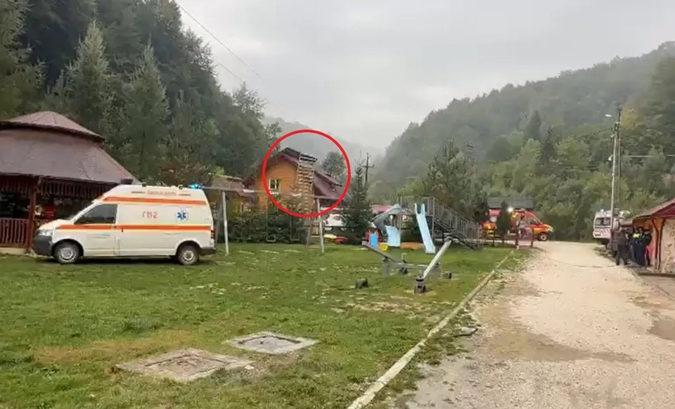 O dubă albă cu inscripții roșii este parcată pe un teren de iarbă lângă o clădire cu acoperiș în formă de con și un teren de joacă.