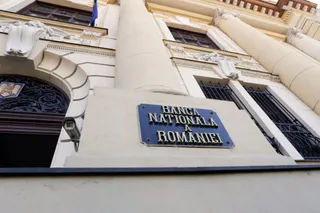 O placă albastră cu textul Banca Națională a României este montată pe fațada unei clădiri cu coloane și ferestre gri.