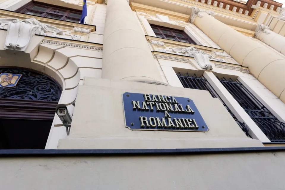 O placă albastră cu textul Banca Națională a României este montată pe fațada unei clădiri cu coloane și ferestre gri.